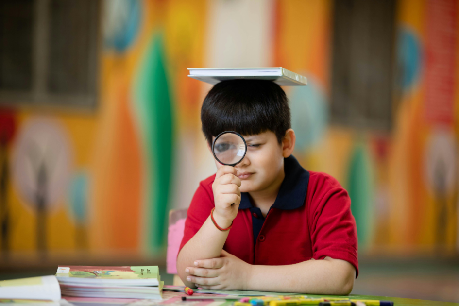 Niño distraido con una lupa y un libro sobre la cabeza mientras estudia