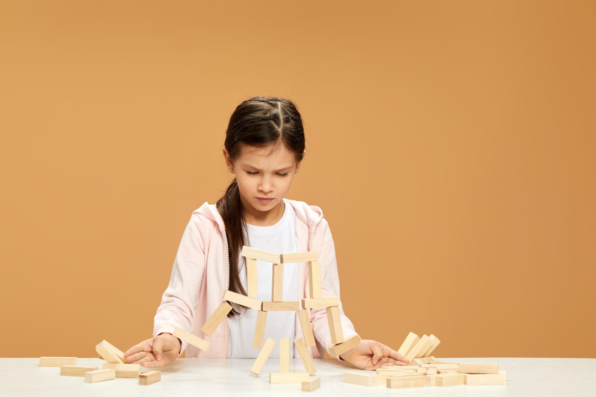 niña con cara de frustración ante una torre de bloques derrumbada